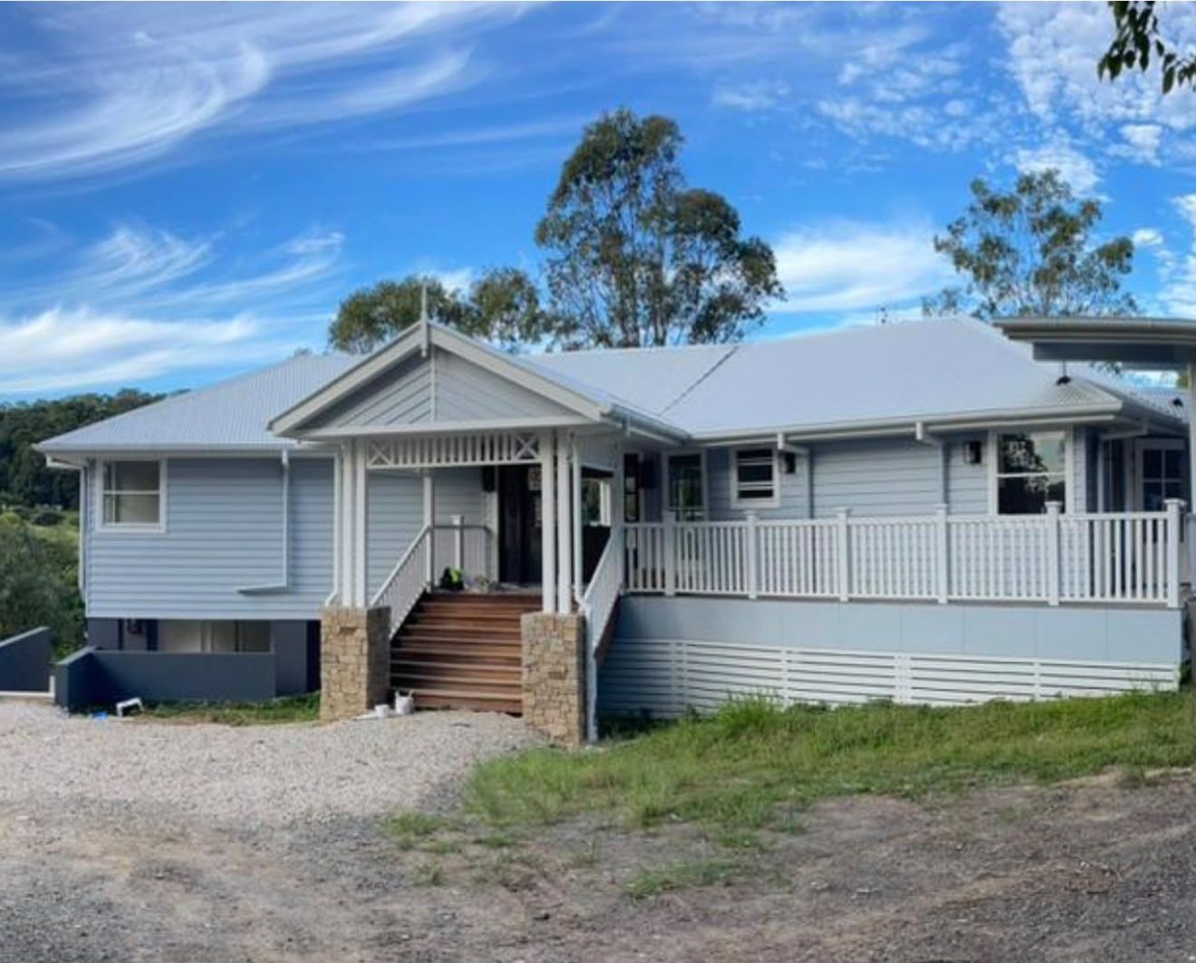 A weatherboard Queenslander home freshly painted in soft coastal grey with white trim
