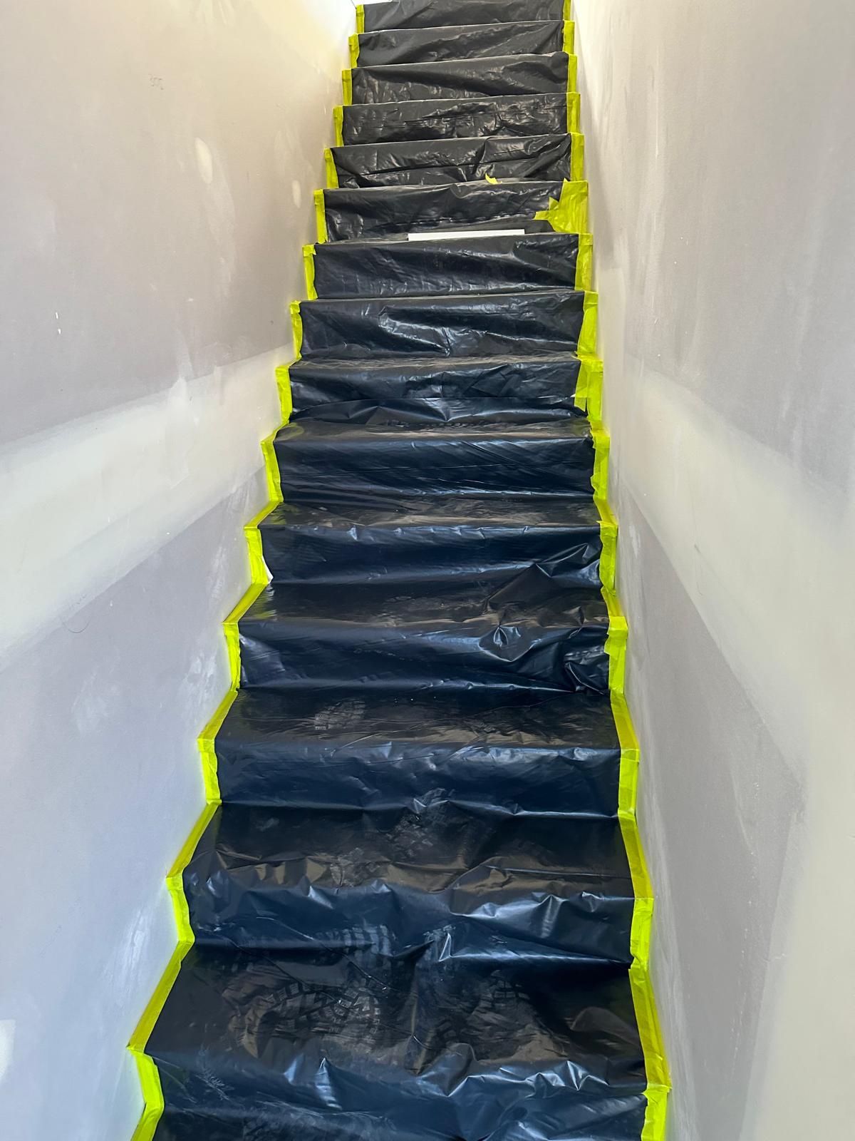 Staircase masked with plastic sheeting and yellow tape ready for painting